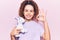Beautiful kid girl with curly hair holding animal doll toy doing ok sign with fingers, smiling friendly gesturing excellent symbol