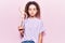 Beautiful kid girl with curly hair holding small wooden manikin thinking attitude and sober expression looking self confident