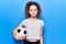 Beautiful kid girl with curly hair holding soccer ball thinking attitude and sober expression looking self confident