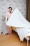 Beautiful lady in purl coral white robe posing holding blanket on the bed in white interior bedroom