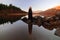 Beautiful lady with red hair, wearing a black cloak, reflected in the still waters of a lake