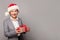 Beautiful lady in red Santa hat holding Christmas gift box and celebrating New Year, studio background