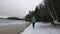 A beautiful lady traveler enjoying the view of a peaceful winter wonderland while walking by the frozen lake in the middle of a fo