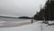 A beautiful lady traveler enjoying the view of a peaceful winter wonderland while walking by the frozen lake in the middle of a fo