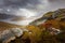 Beautiful lake behind a cliff and surrounded by cliffs and mounts under cloudy dark sky