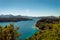 Beautiful lake with intense turquoise shores, a wooded island in the middle and snowy mountain ranges in the background.