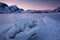 Beautiful landscape cracking ice, frozen sea coast with mountain ridge background at sunset in Lofoten Islands, winter season,