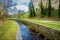 Beautiful landscape with  narrow canal  lined with few bare trees, concrete path  and cypress trees