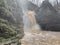 Beautiful landscape of powerful muddy waterfall in mountainous terrain. Dirty mountain waterway flows down and splashes.