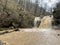 Beautiful landscape of powerful muddy waterfall in mountainous terrain. Dirty mountain waterway flows down and splashes.