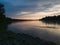 Beautiful landscape with river, forested riparian zone and hazy mountains in distance during cloudy evening in long exposure