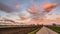 Beautiful landscape with road, fields and blue sky covered partially with fluffy colorful clouds in the background