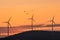 Beautiful landscape with silhouettes of three wind turbines on a hill in the sunset light and birds