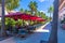 Beautiful landscape view of outdoor cafe. Blue chairs under red umbrellas on green trees and blue sky background.