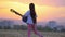 Beautiful landscape view at sunset. funny little girl musician playing the guitar walks outdoors dandelions field away from town b