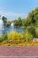 Beautiful large pond with lush fountains, surrounded by tall green trees and flower beds with flowers against the blue