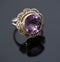 Beautiful large purple shining gemstone ring photo with gold colored band on a black shiny surface