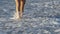 Beautiful legs of a young woman walking on a beach with wave foams rolling around her feet