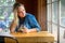 Beautiful lifestyle portrait of a woman at a brewery with a pint of craft cider, looking out window, wooden table