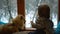 Beautiful little blond toddler and his fluffy pomeranian spitz are looking on the snow through window while sitting on