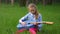 Beautiful little blonde girl sitting in green grass playing jeans guitar outdoor. spring season in countryside