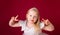 Beautiful little blonde princess dancing in luxury white and silver dress isolated on red background. Funny face, different