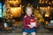 A beautiful little blonde received a sweet Christmas gift and laughs happily sitting on a wooden table in a decorated house