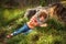 Beautiful little girl in black and white scarf, jeans and orange pullover lies on the ground on meadow near big stump and big