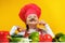 Beautiful little girl chef on a yellow background. A child prepares a vegetable salad, fooling around and making a mustache