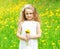 Beautiful little girl child on meadow with yellow dandelion flowers in sunny summer