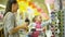 Beautiful Little Girl is Choosing a Sunglasses in the Supermarket. Woman with Long Dark Hair and Yellow Backpack Helps