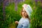 A beautiful little girl in a dress and hat in a field of lupins. Purple lupine flowers are blooming. The concept of nature.