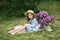 Beautiful little girl in dress with Lilac bouquet in garden. Spring blossom. Cute Smile young girl  in straw hat with purple flowe