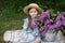 Beautiful little girl in dress with Lilac bouquet in garden. Spring blossom. Cute Smile young girl  in straw hat with purple flowe