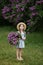 Beautiful little girl in dress with Lilac bouquet in garden. Spring blossom. Cute Smile young girl  in straw hat with purple flowe