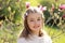 Beautiful little girl with handmade hair wreath on her head smiling looking at camera in the blooming spring garden