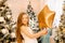 Beautiful little girl laughs and stands near the Christmas trees with a star balloon. concept of happy childhood, making a wish fo