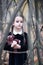 Beautiful little girl with long brunette hair, dressed in black velvet dress walks in fall forest with handmade bear toy.