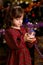 Beautiful little girl in red festive dress holds christmas glass magic ball near christmas tree