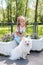 Beautiful little girl sitting on bench in park with her adorable white Pomeranian dog
