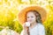 Beautiful little girl sitting in a straw hat in a field and eating marshmallows, picnic in a field