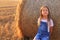 Beautiful little girl stands near a haystack in a summer field