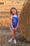 Beautiful little girl stands near a haystack in a summer field