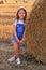 Beautiful little girl stands near a haystack in a summer field