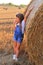 Beautiful little girl stands near a haystack in a summer field