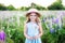 Beautiful little girl in a straw hat and dress holds a dandelion in a flowering field. Nature concept. A smiling girl is playing o
