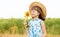 Beautiful little girl in straw hat with fluttering hair hold sunflower flower, walking outdoor in summer holiday