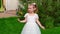 beautiful little girl in white dress stands and says something on green lawn