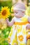 Beautiful little girl in a yellow dress smelling a sunflower