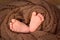 Beautiful little heels of a newborn baby wrapped in a brown knitted piece of cloth